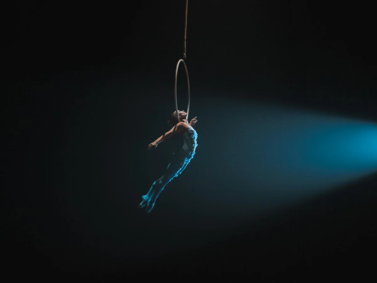 An aerial hoop artist lit by a single spotlight against a dark stage (representative photograph, not this venue's own cast)