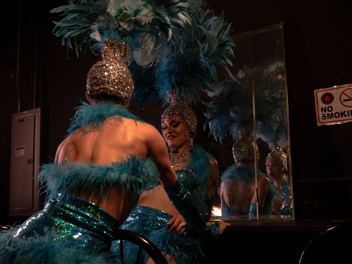 Two showgirls backstage in sequinned, feathered costumes, one reflected in a mirror (representative photograph, not this venue's own cast)